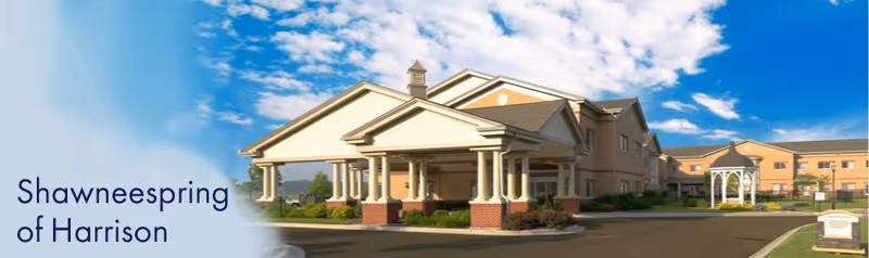 Exterior view of Shawneespring Skilled Nursing Facility showing a large building with a covered entrance supported by columns, a gazebo on the right side, and a clear blue sky with some clouds above.