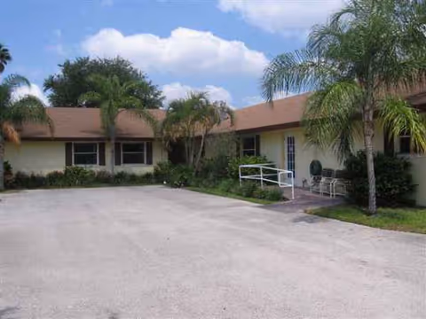 Single-story facility exterior with palm trees, ramp, and chairs near the entrance.