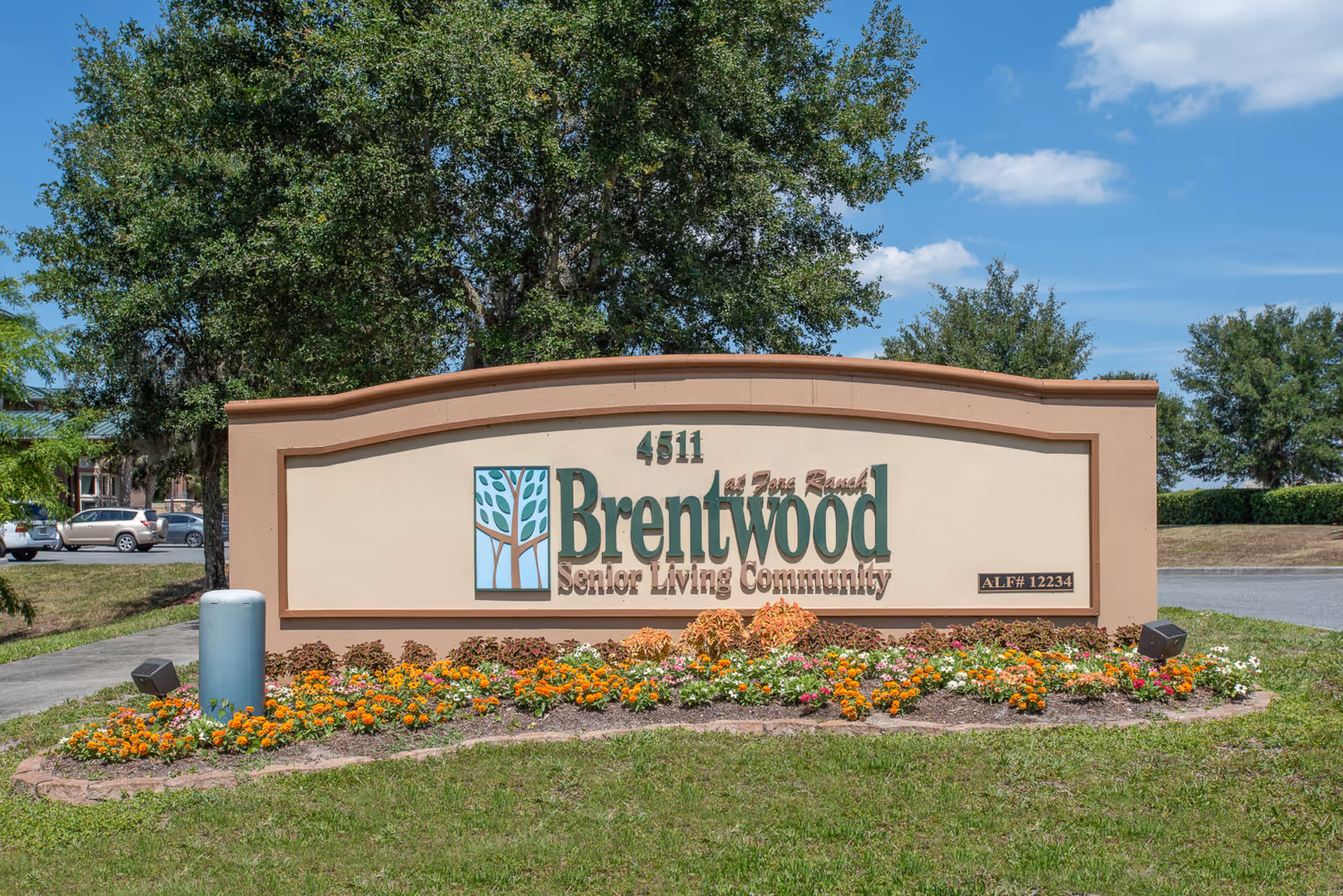 Outdoor sign for Brentwood at Fore Ranch Senior Living Community with flowers planted in front and trees in the background under a blue sky with some clouds.