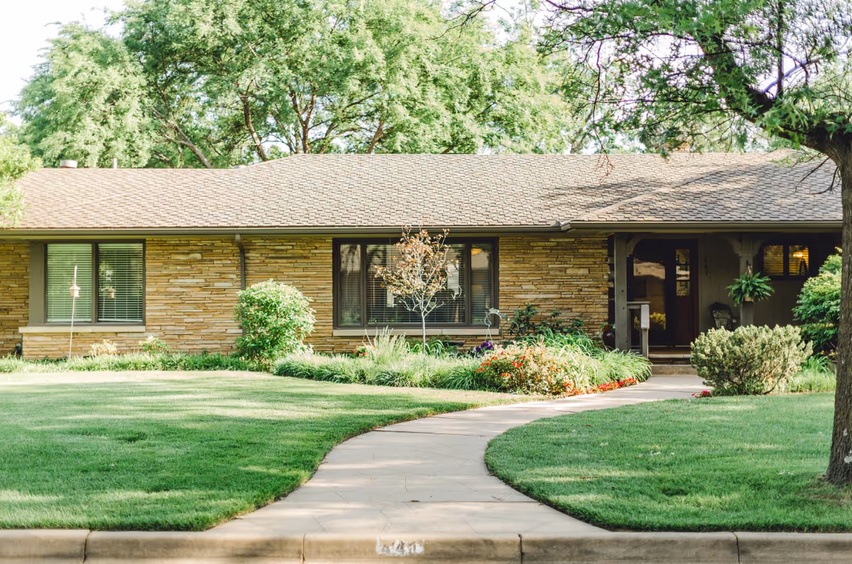 Single-story ranch-style house with a curved walkway, manicured lawn, and landscaped front yard.