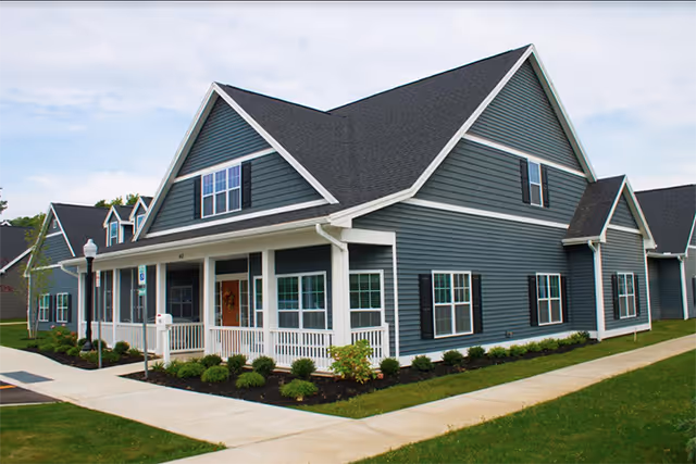 Blue senior living building with a front porch, windows, and neatly landscaped lawn.