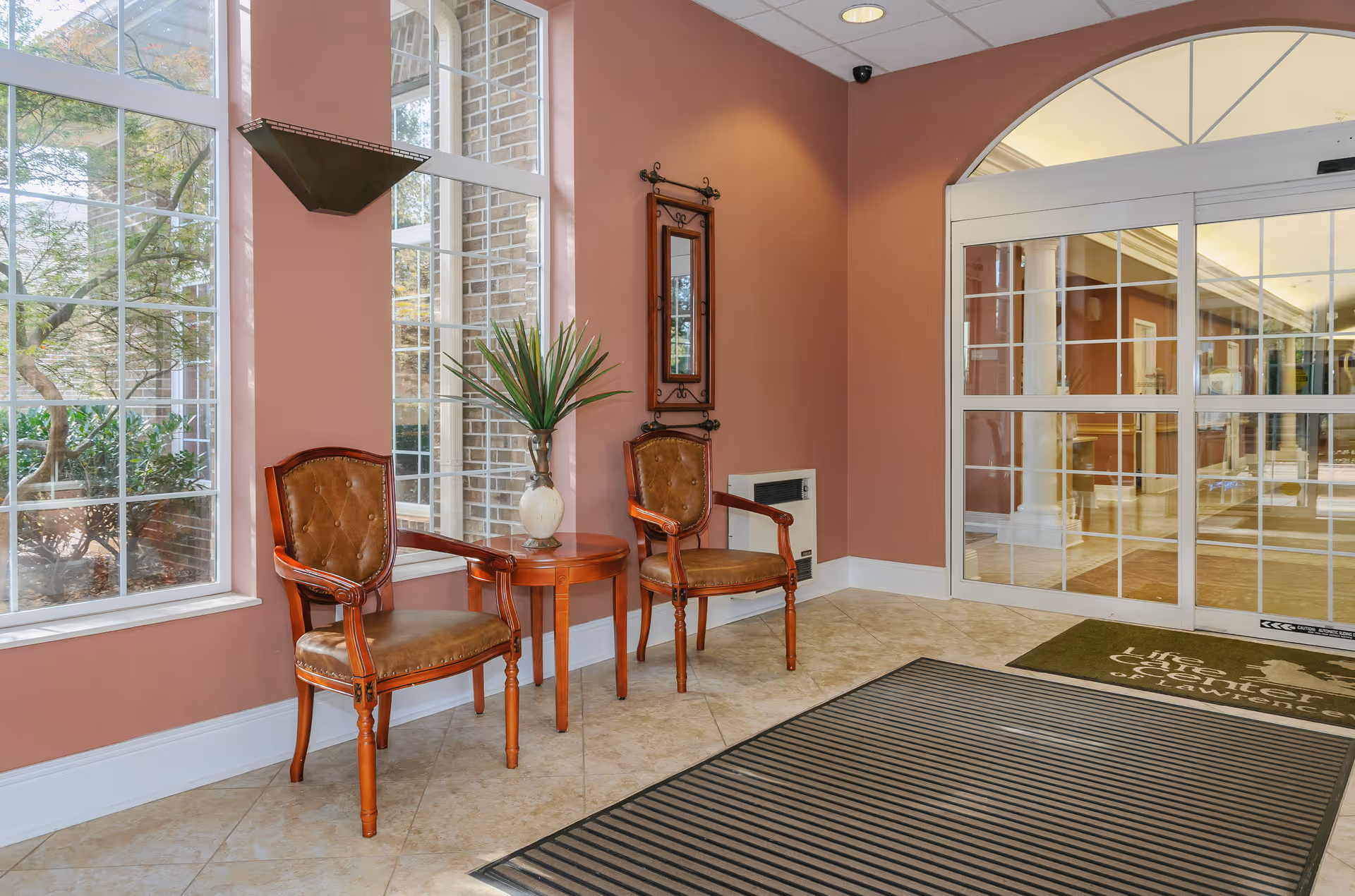 Entrance lobby with two wooden chairs and a small table beside large windows and sliding glass doors.