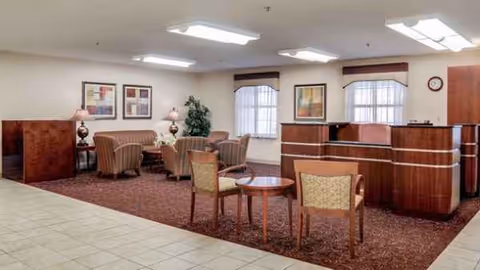 A spacious indoor lobby with seating, tables, lamps, and a curved wooden reception desk.