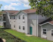 Two-story beige senior living building with gray siding and a green door, outdoors.