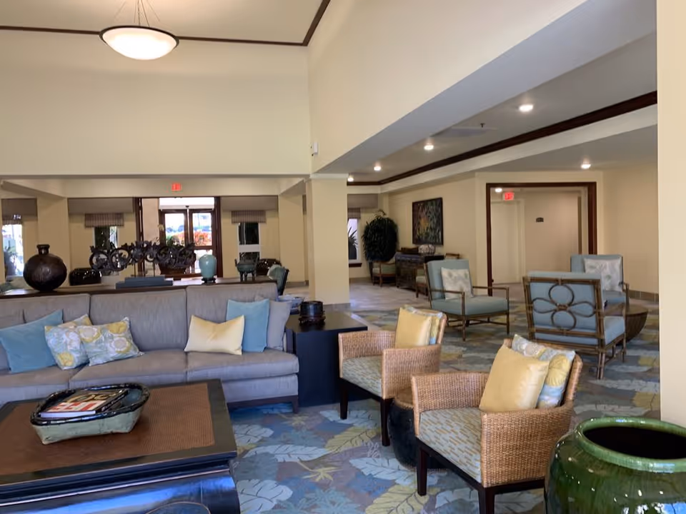 Spacious furnished lounge with sofas, armchairs, decorative vases, and patterned carpet in a senior living facility.