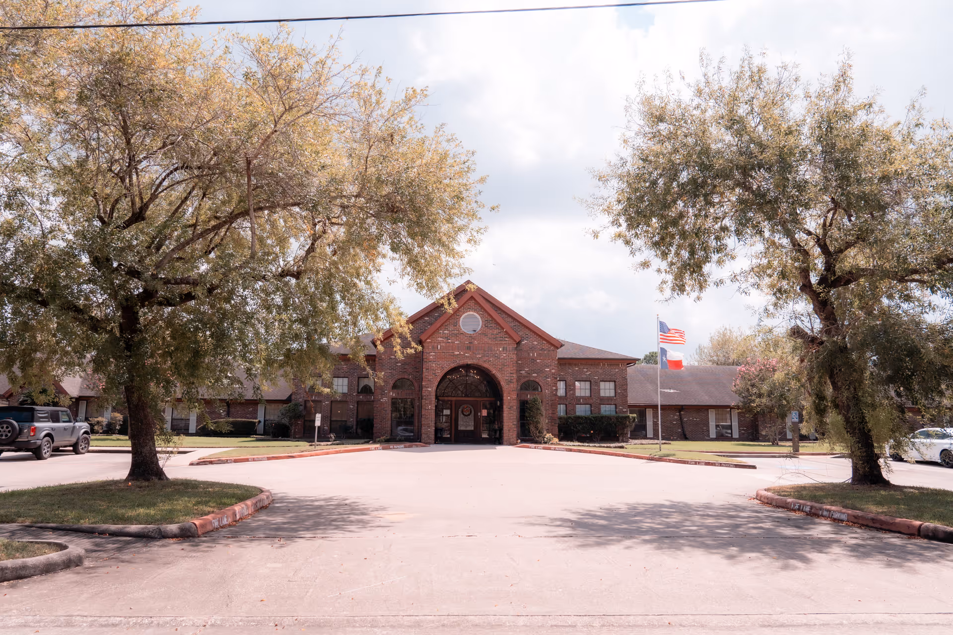 Front view of Regency Village of Webster, showcasing the brick facade, entrance archway, and surrounding trees.