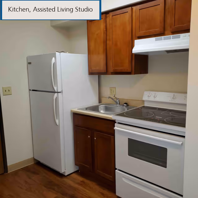 Small assisted living studio kitchen with a white refrigerator, electric stove, stainless sink, and wooden cabinets.