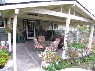 Covered front porch of a senior living facility with plants and outdoor seating.