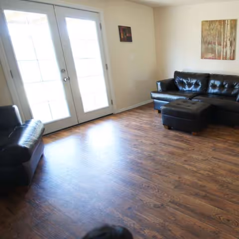 Interior living room with leather sofas, ottoman, and French doors.
