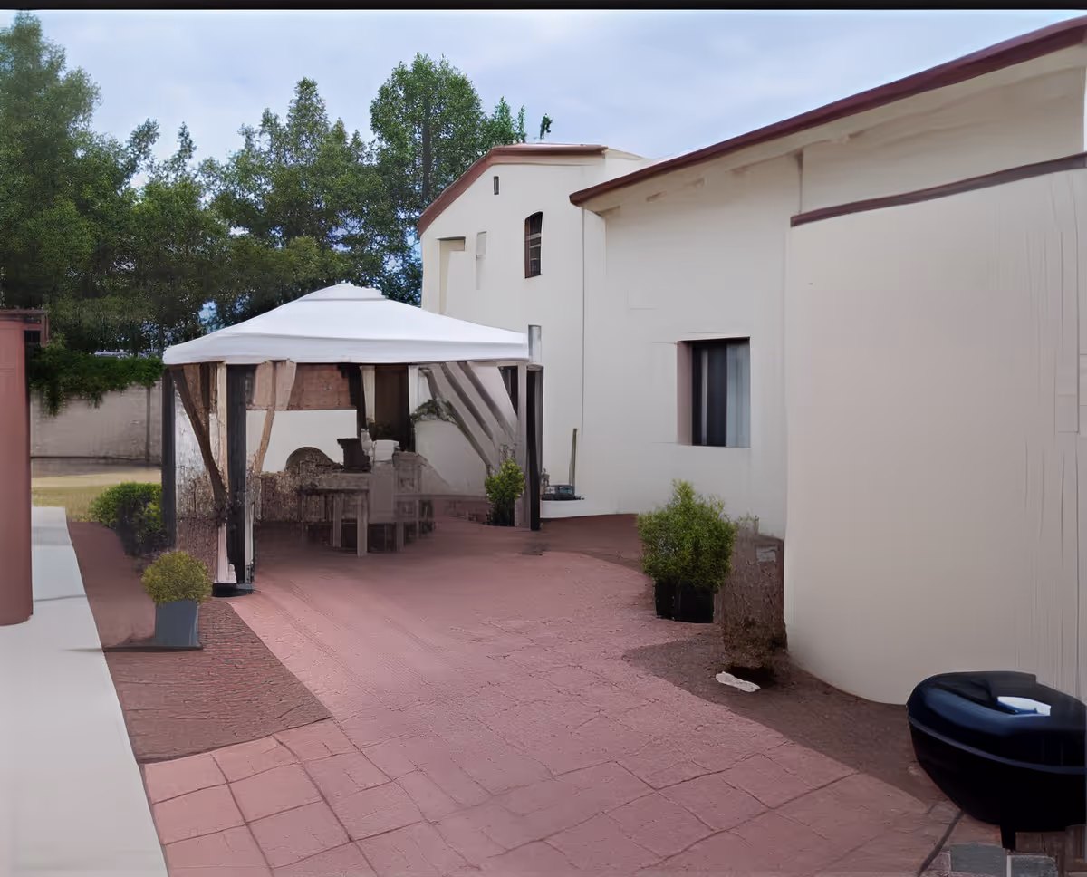 Outdoor patio area at Autumn Years Care Center featuring a white canopy tent with seating underneath, surrounded by potted plants and trees, adjacent to a beige building with a window.