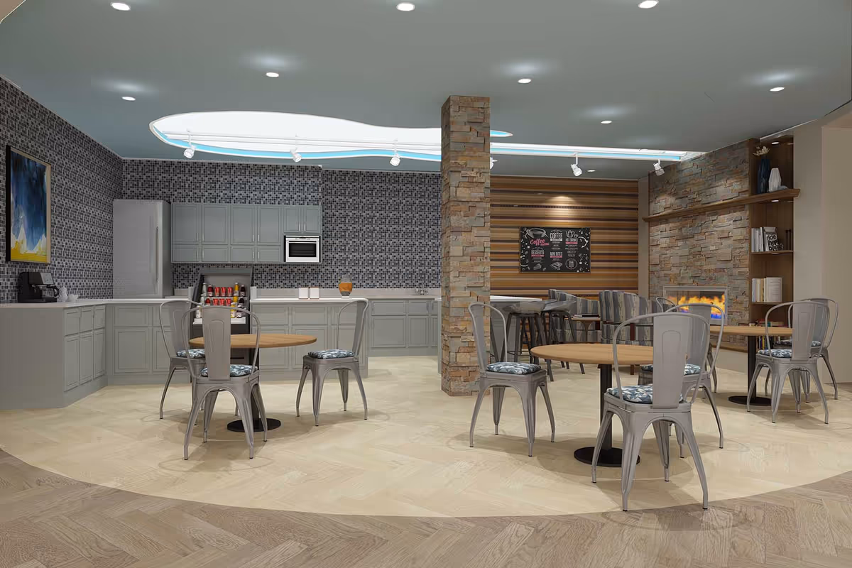Open communal dining area with round tables and metal chairs in front of a kitchenette and a stone-accented seating area with a fireplace.