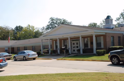 Brick Dugan Memorial Home entrance with columns and parked cars.