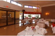 Well-lit dining room with multiple tables set for service, chandeliers, and large windows/doors.
