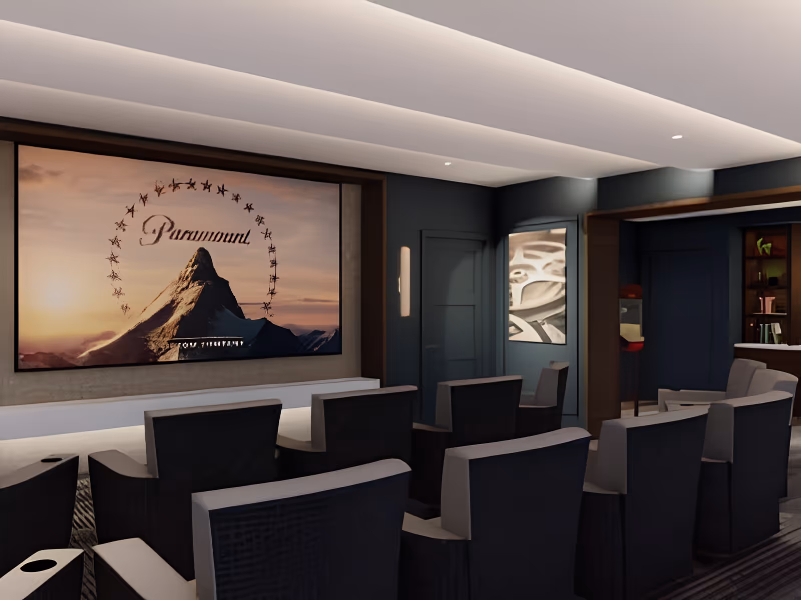 Small theater room with rows of upholstered recliner seats facing a large screen showing the Paramount logo.