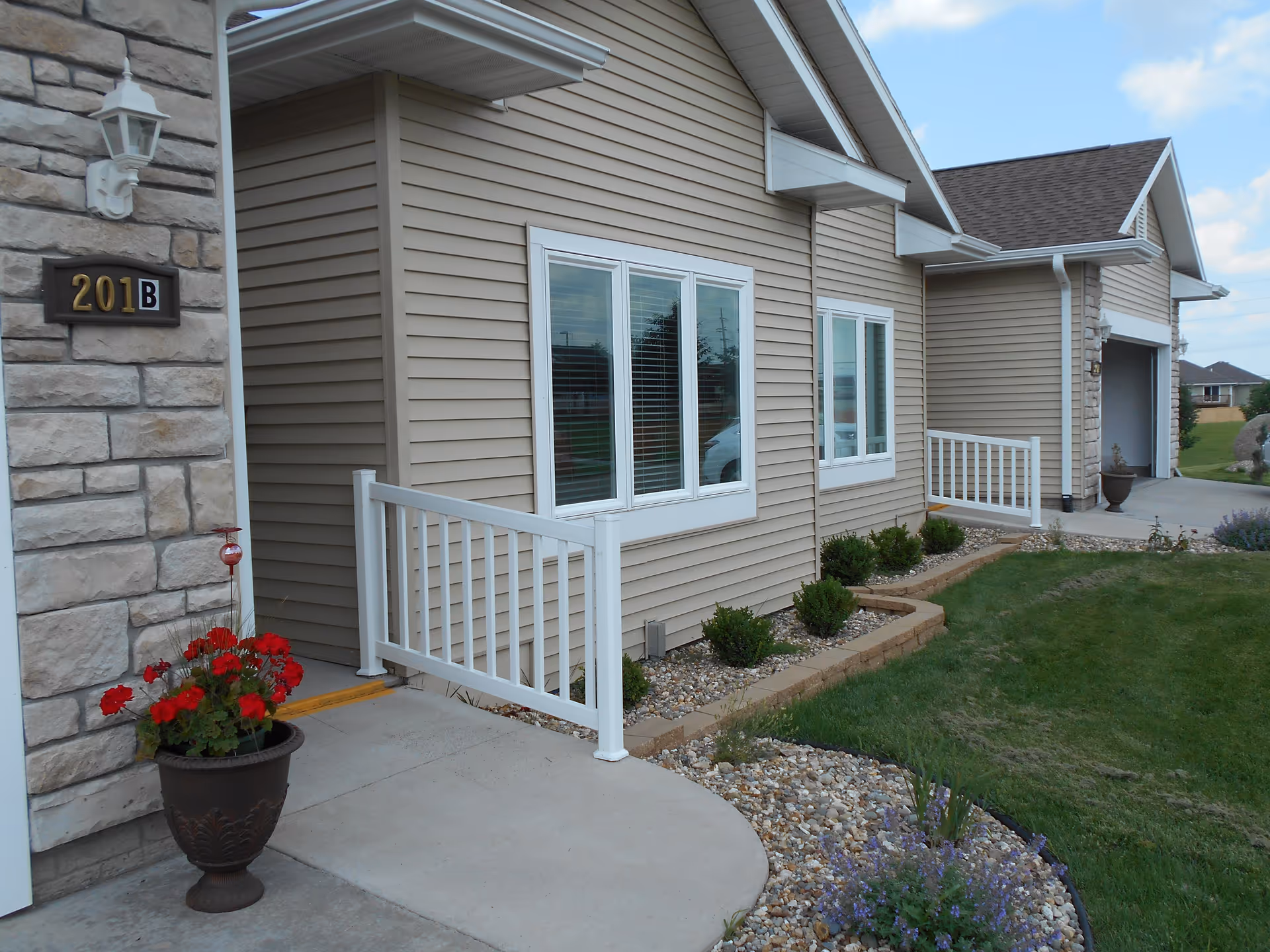 Front exterior of a beige single-story unit with white railings, a potted red flower, and house number 201B.