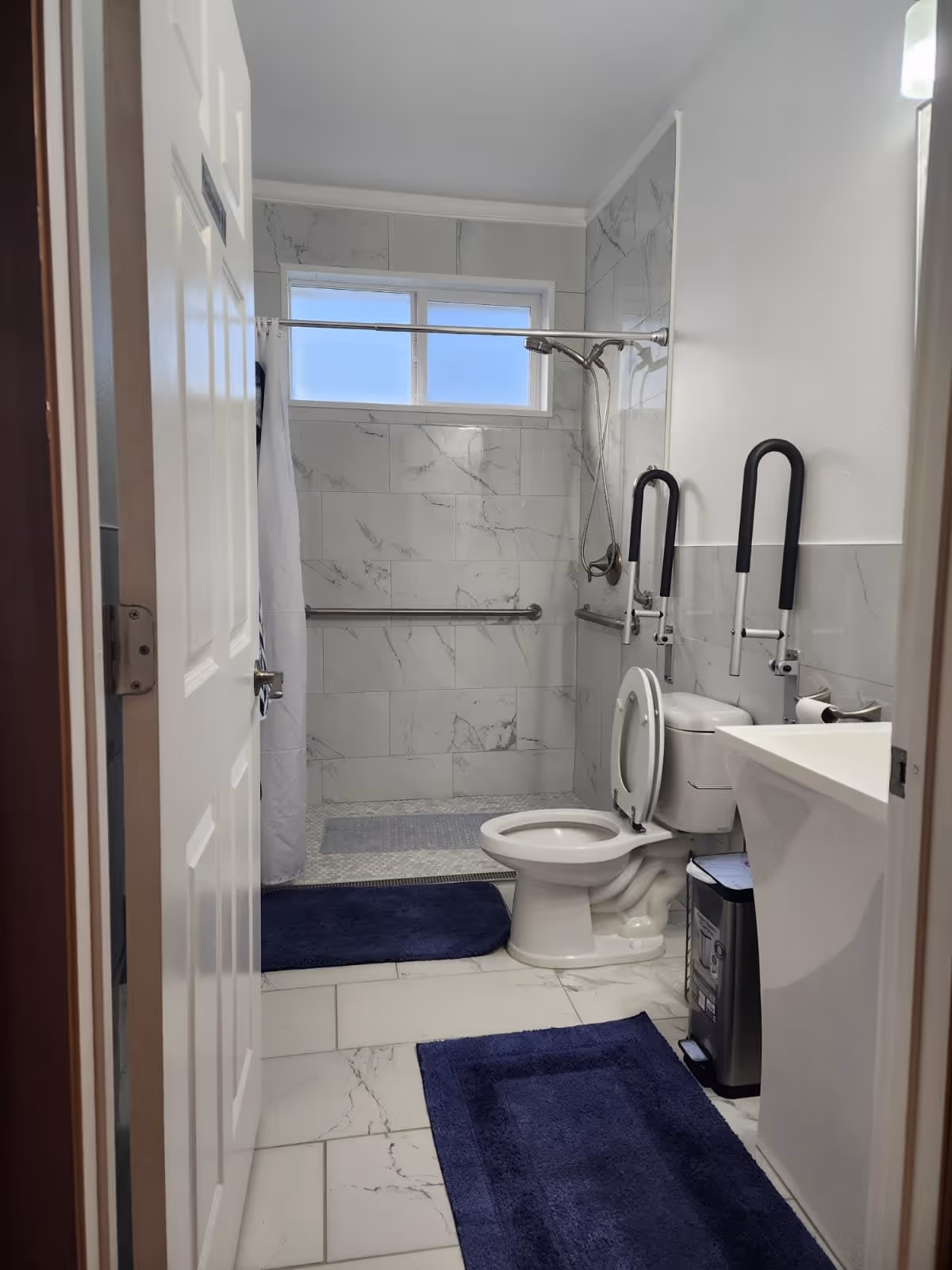 Accessible bathroom with a toilet, grab bars, a walk-in shower, and blue bath mats.