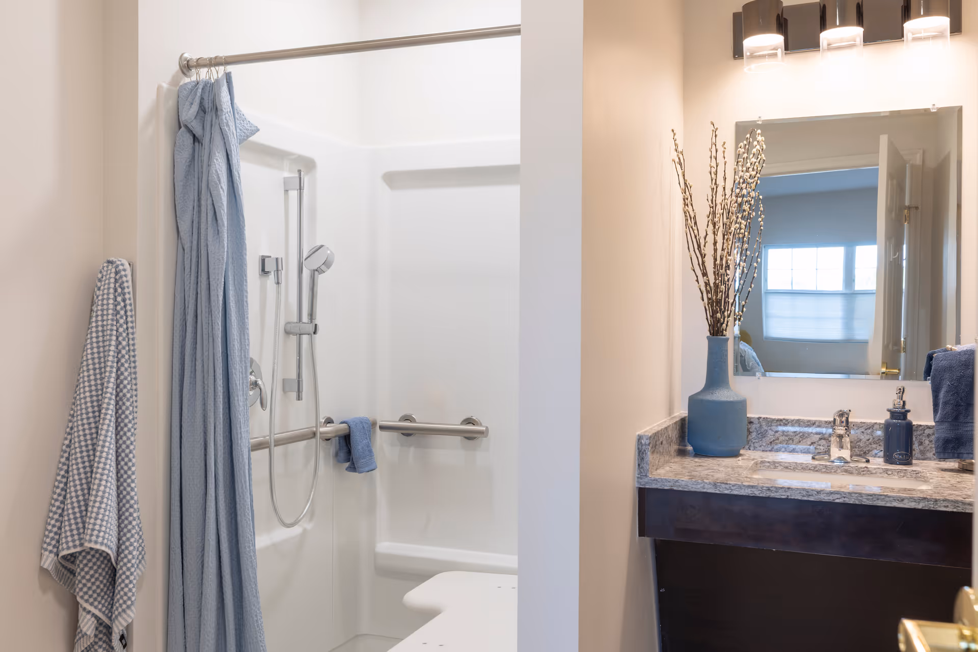 Accessible bathroom with a walk-in shower and grab bar, blue towels, and a vanity with sink and mirror.