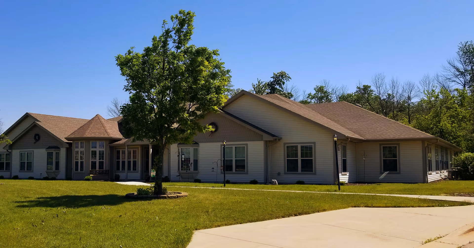 Single-story building with beige siding and brown roof surrounded by green grass and trees under a clear blue sky.