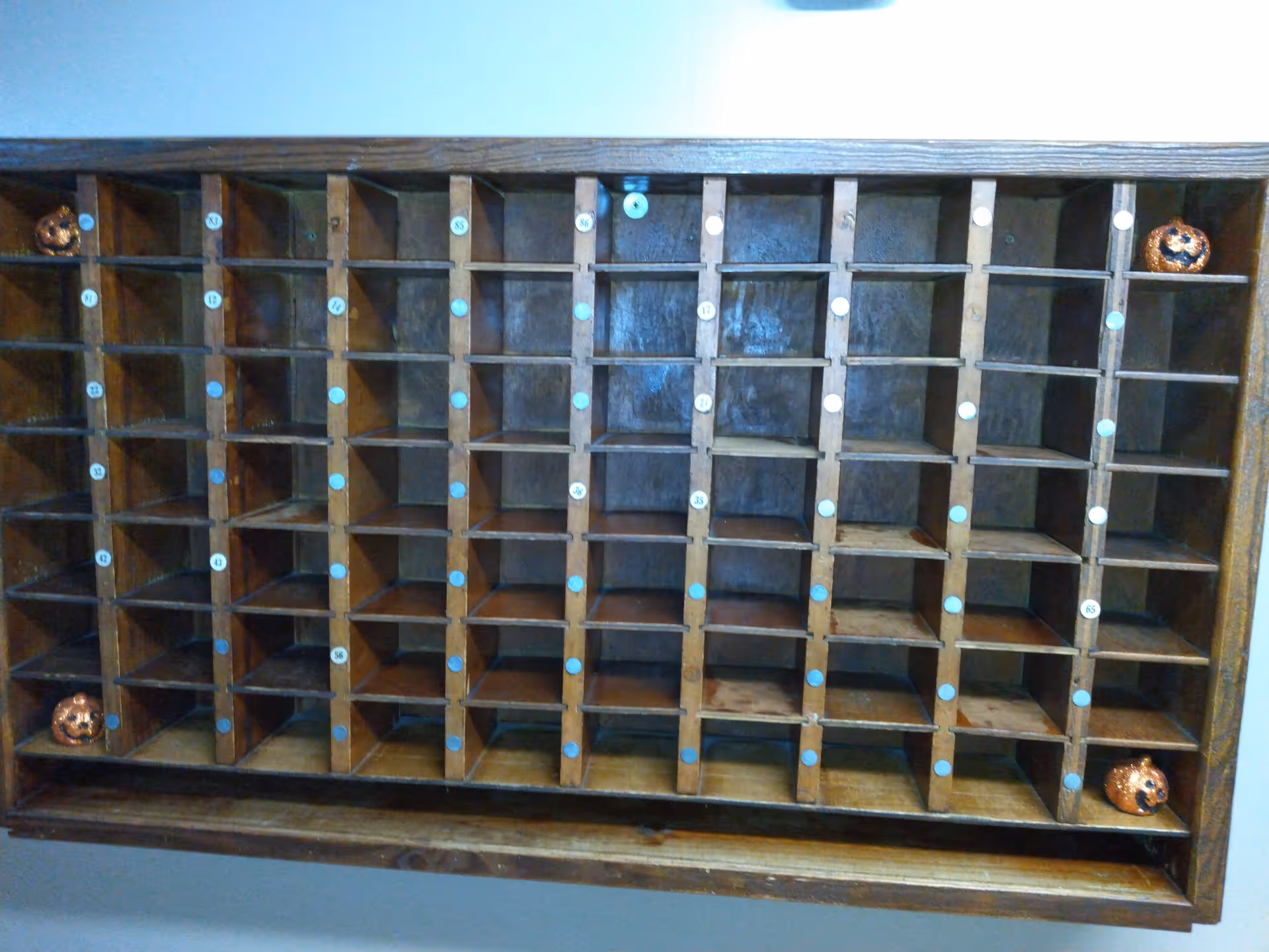 Wooden cubby mail organizer with multiple numbered compartments, some decorated with small pumpkin ornaments.