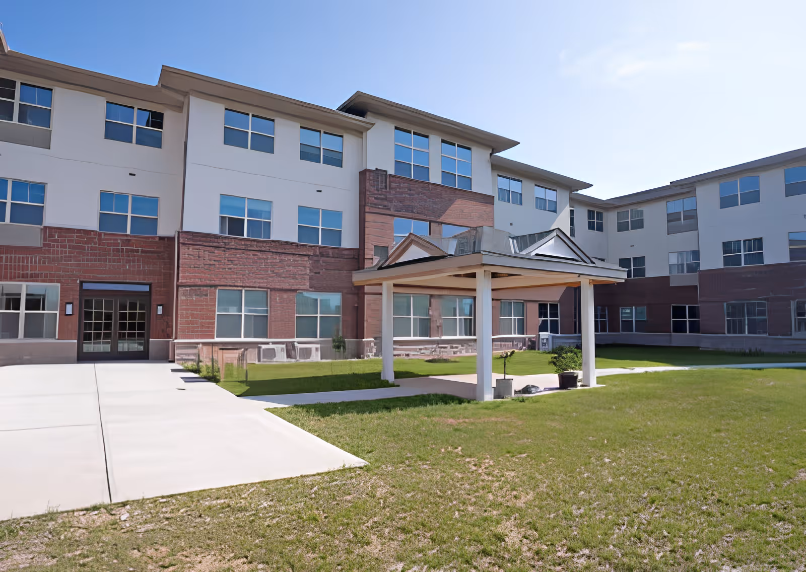 Exterior view of a three-story senior living facility with a covered entrance pavilion and lawn.