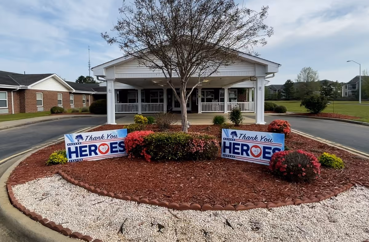 Entrance of Liberty Commons Nursing & Rehabilitation Center featuring flower beds and signs thanking heroes.
