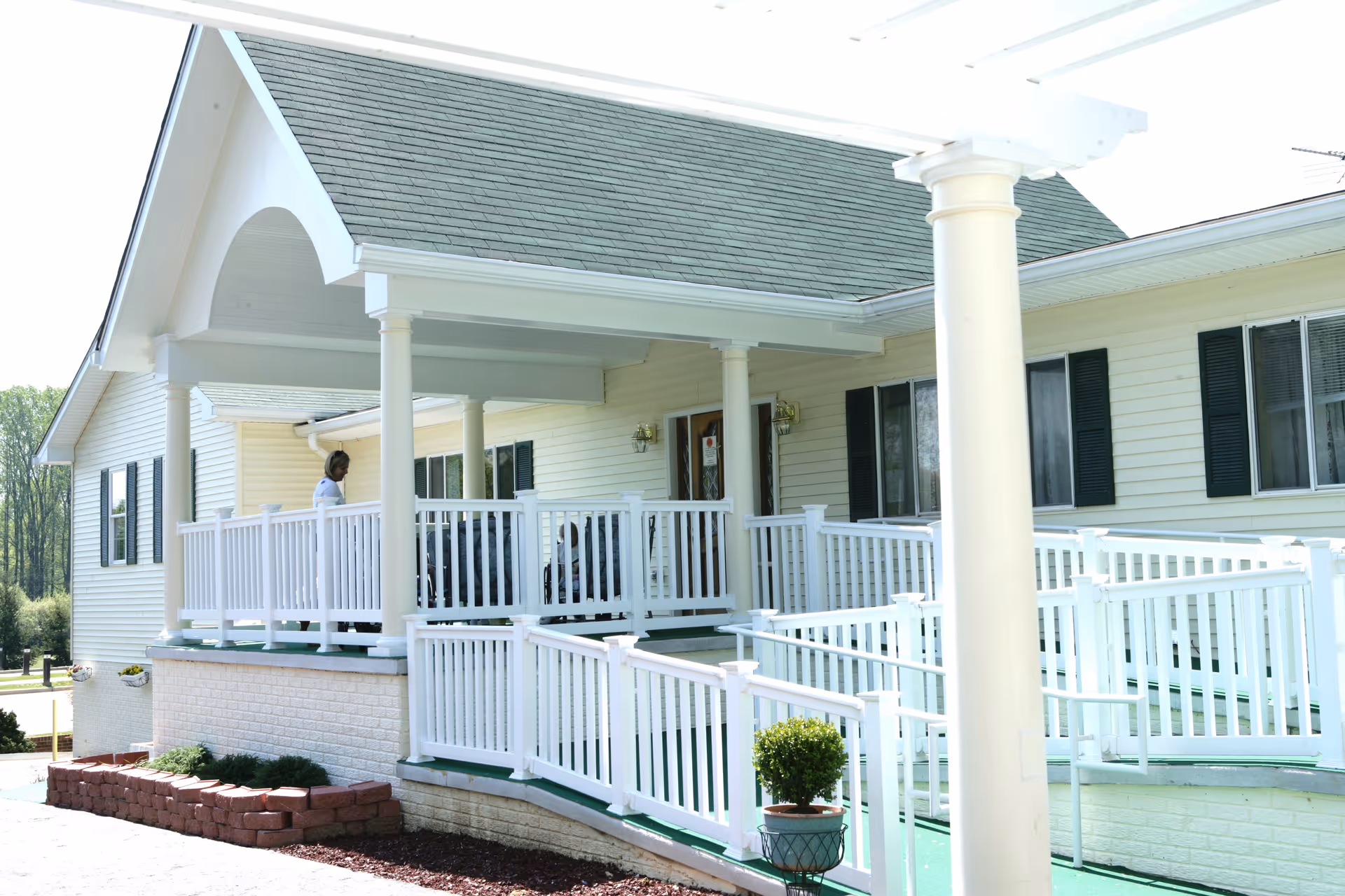 Front entrance of a single-story light-colored building with a covered porch, white railings, and an accessibility ramp.