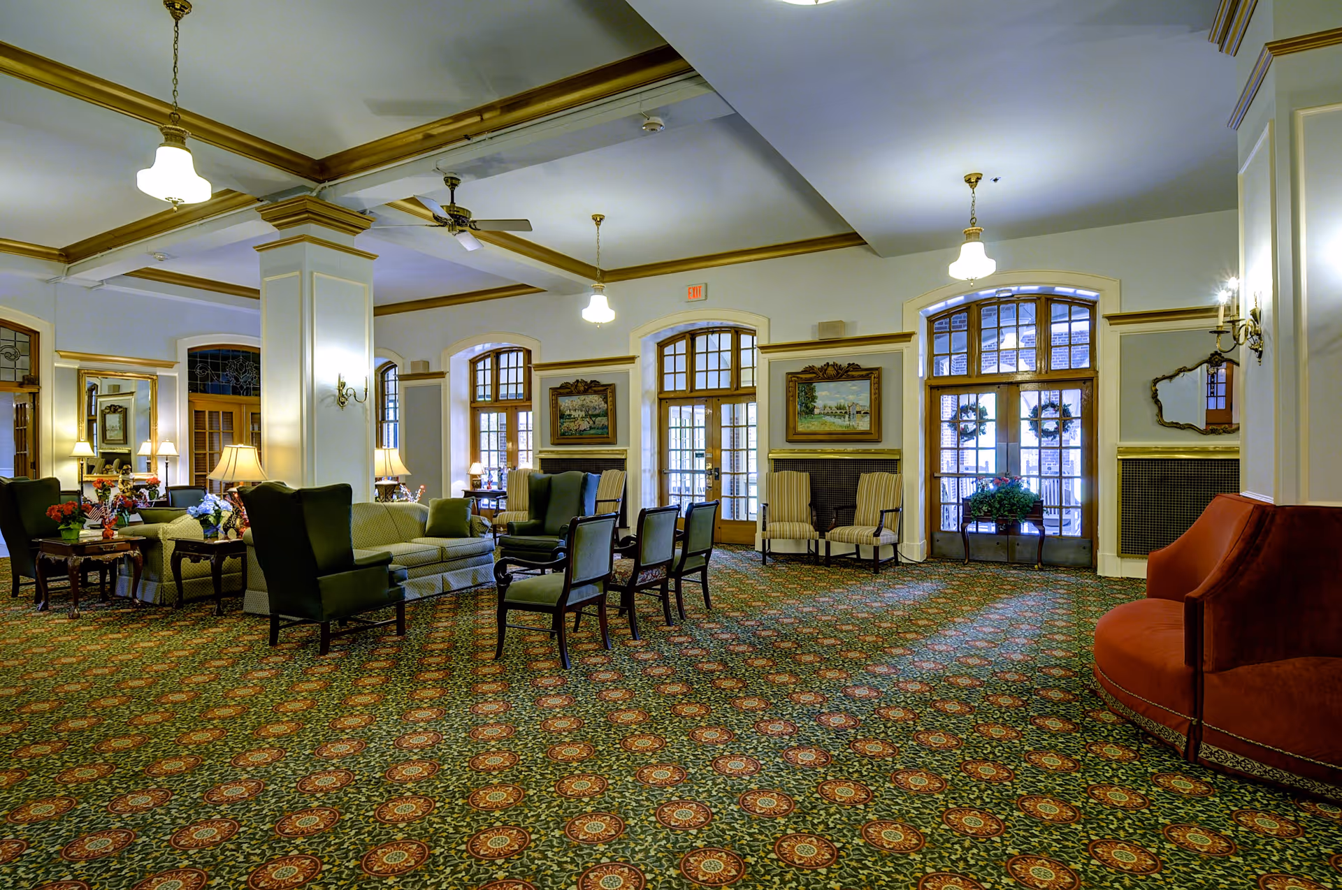 Spacious formal lounge with patterned carpet, multiple sofas and armchairs, chandeliers, and large arched windows and doors.