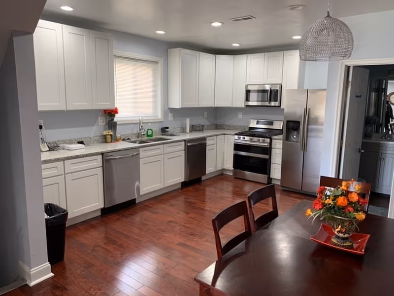 Bright kitchen with white cabinets, stainless appliances, dark wood dining table, floral centerpiece.