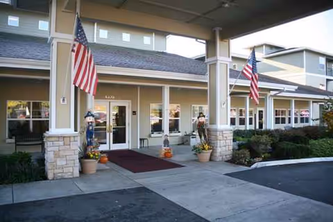 Senior living facility entrance at Woodland by Bonaventure with flags, pumpkins, planters, and a covered porch.