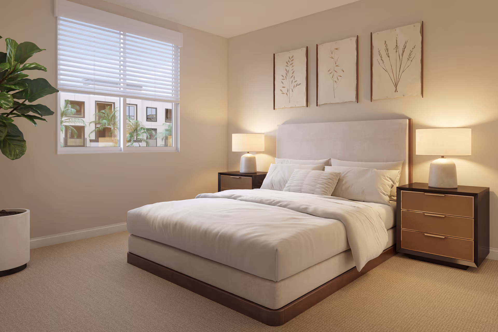 A cozy bedroom with a large bed featuring white bedding and multiple pillows. There are two bedside tables with matching lamps on each side of the bed. Above the bed, three framed botanical prints are hung on the wall. A large window with white blinds allows natural light to enter the room, and a potted plant is placed in the corner near the window.