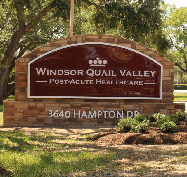 Stone entrance sign reading "Windsor Quail Valley Post-Acute Healthcare" with the address 3640 Hampton Dr set among trees and landscaping.