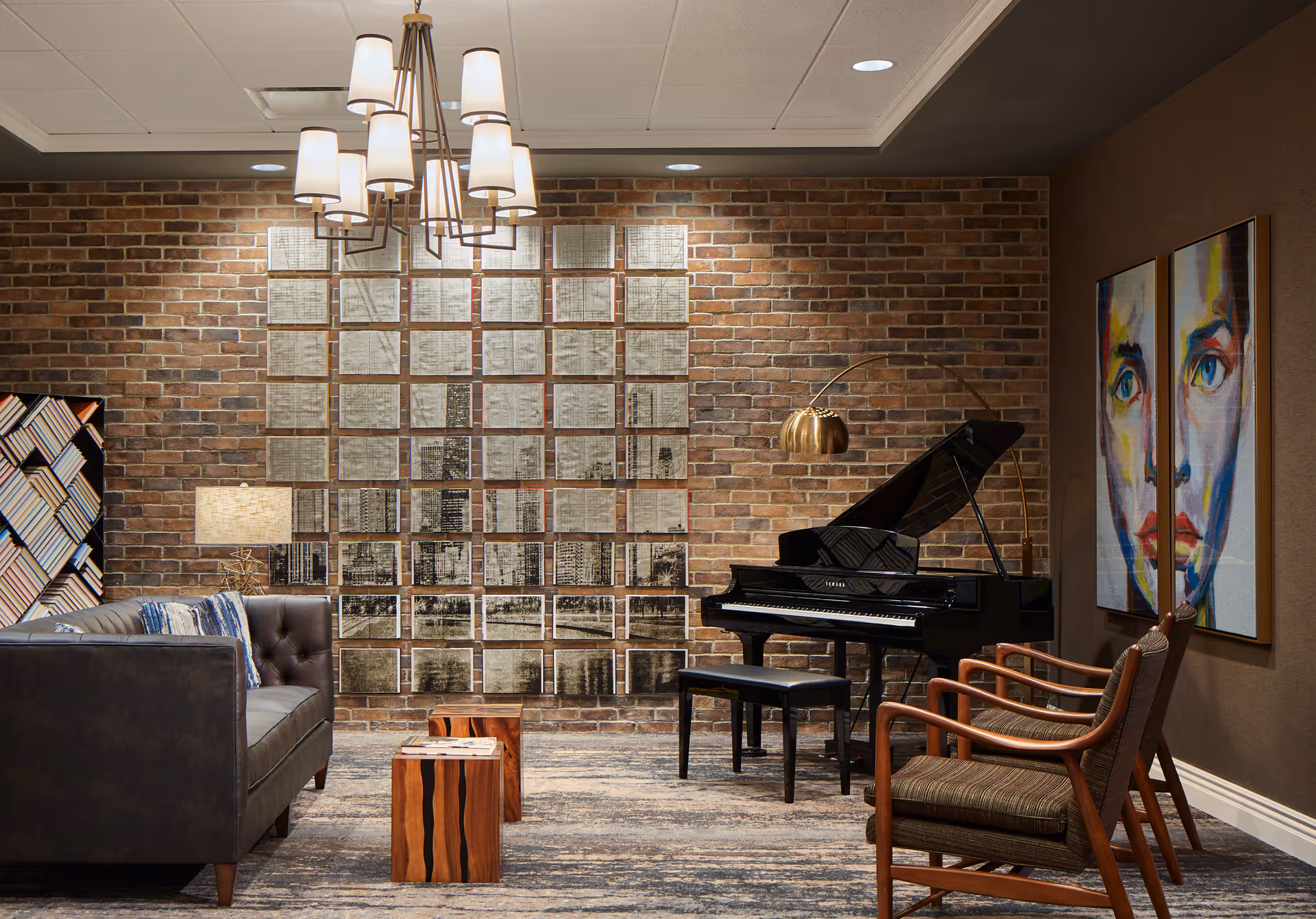 Cozy interior lounge with a brick accent wall, grand piano, seating area, modern chandelier, and colorful portrait artwork.