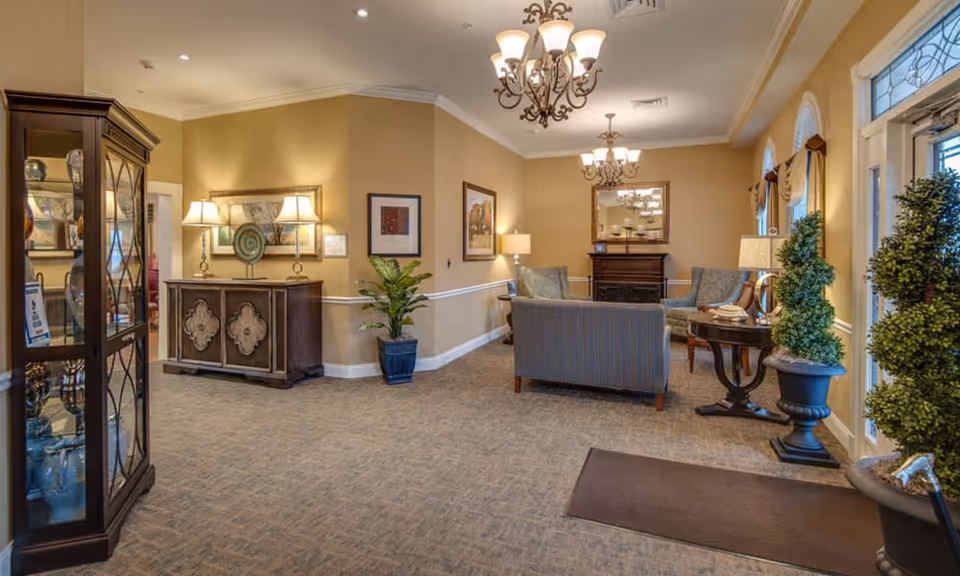 A cozy lobby area featuring comfortable seating, decorative plants, and elegant lighting fixtures, with a stylish cabinet displaying decorative items.