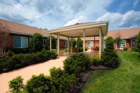 Exterior courtyard of a brick senior living facility with a covered seating area and landscaped paths.