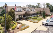 Front entrance of a senior living building with landscaped walkways, a flagpole, and parked cars.