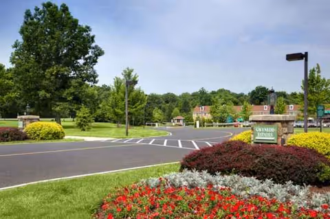 Entrance road and landscaped front of Gwynedd Estates senior living, with sign and greenery.