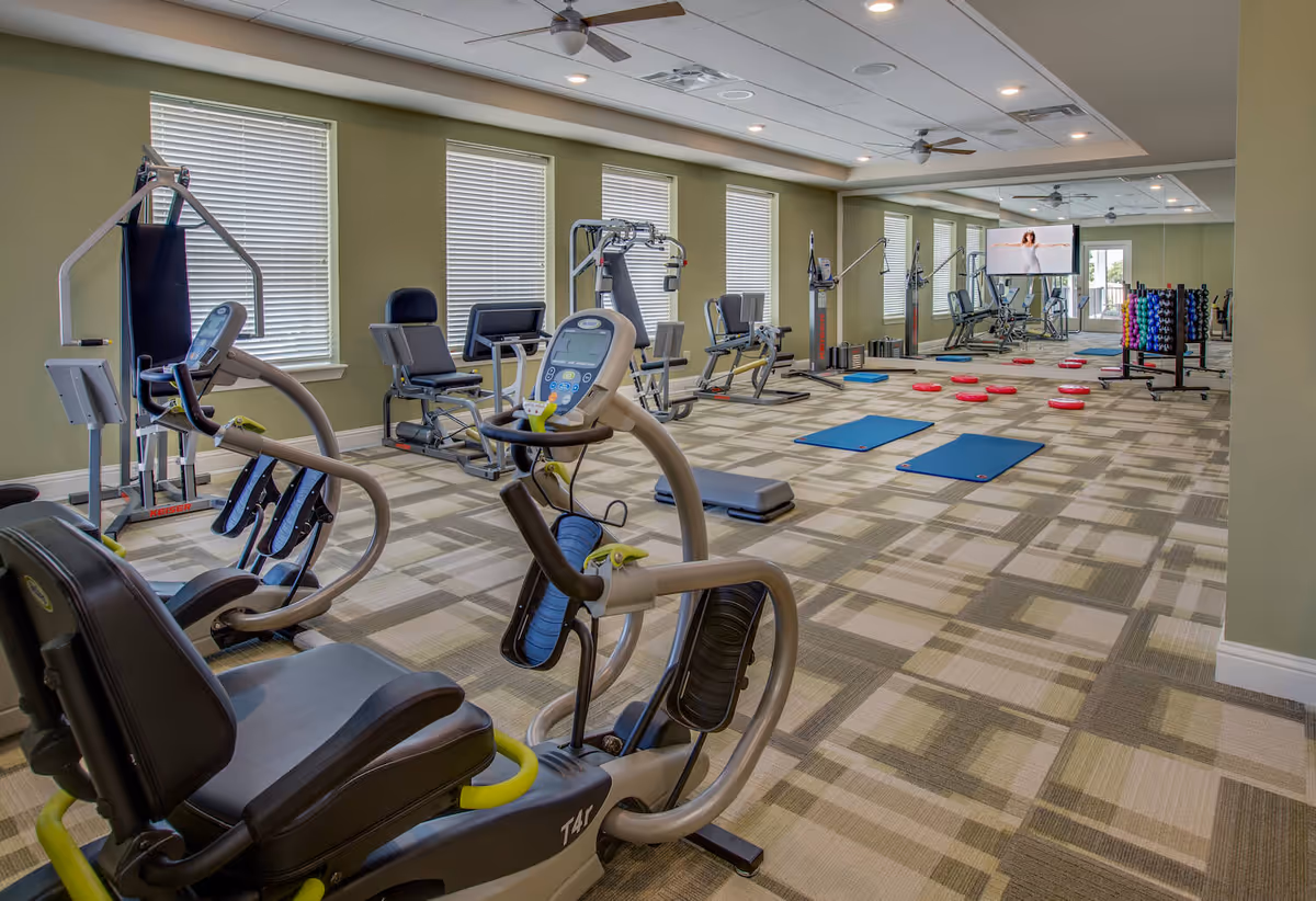Bright indoor fitness room with cardio and strength machines, exercise mats, balance pads, and free weights.