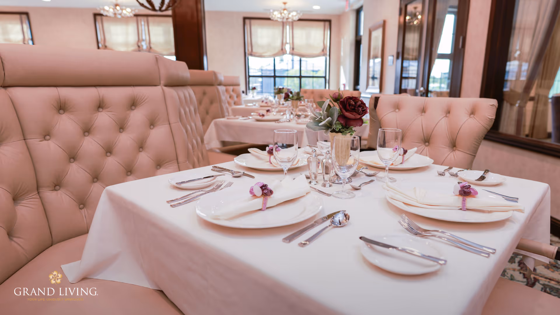 Table set for dining with white linens, glassware, and a floral centerpiece in an elegant room with tufted chairs.