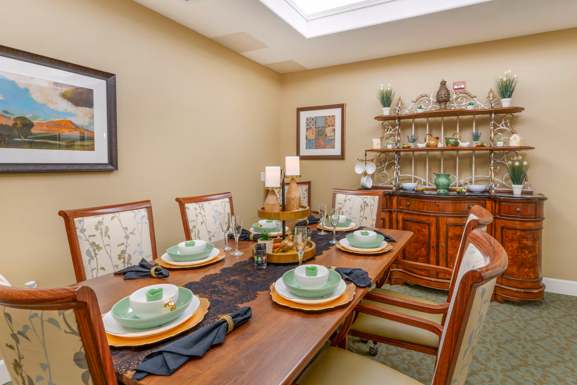 Dining room with a wooden table set for six, upholstered chairs, a decorative buffet and shelving under a skylight.