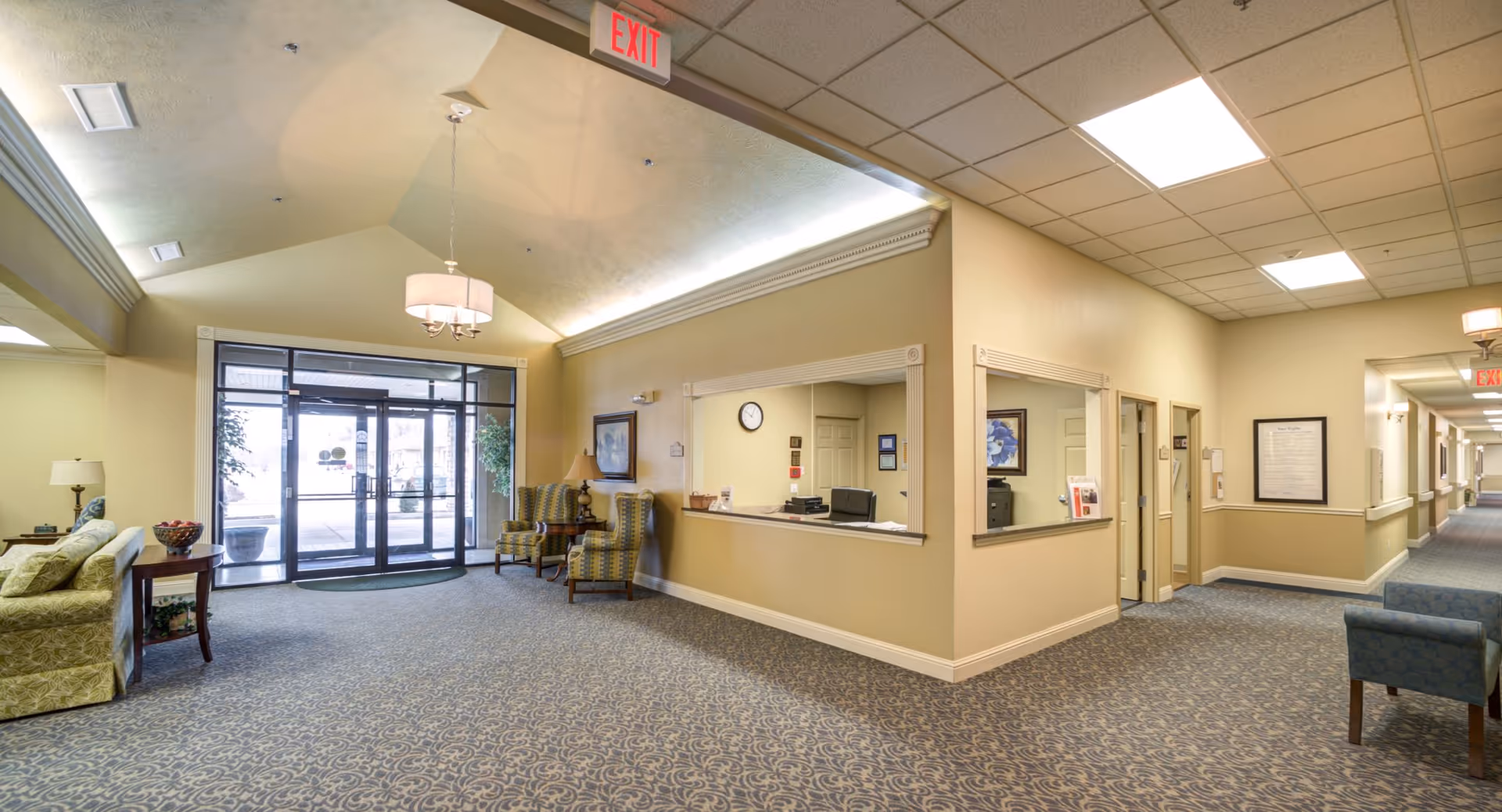 Spacious assisted living lobby with seating, a reception desk, and glass entrance doors.