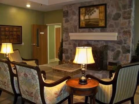 Cozy lounge area with floral-patterned chairs, lamps, and a stone fireplace in a common room.