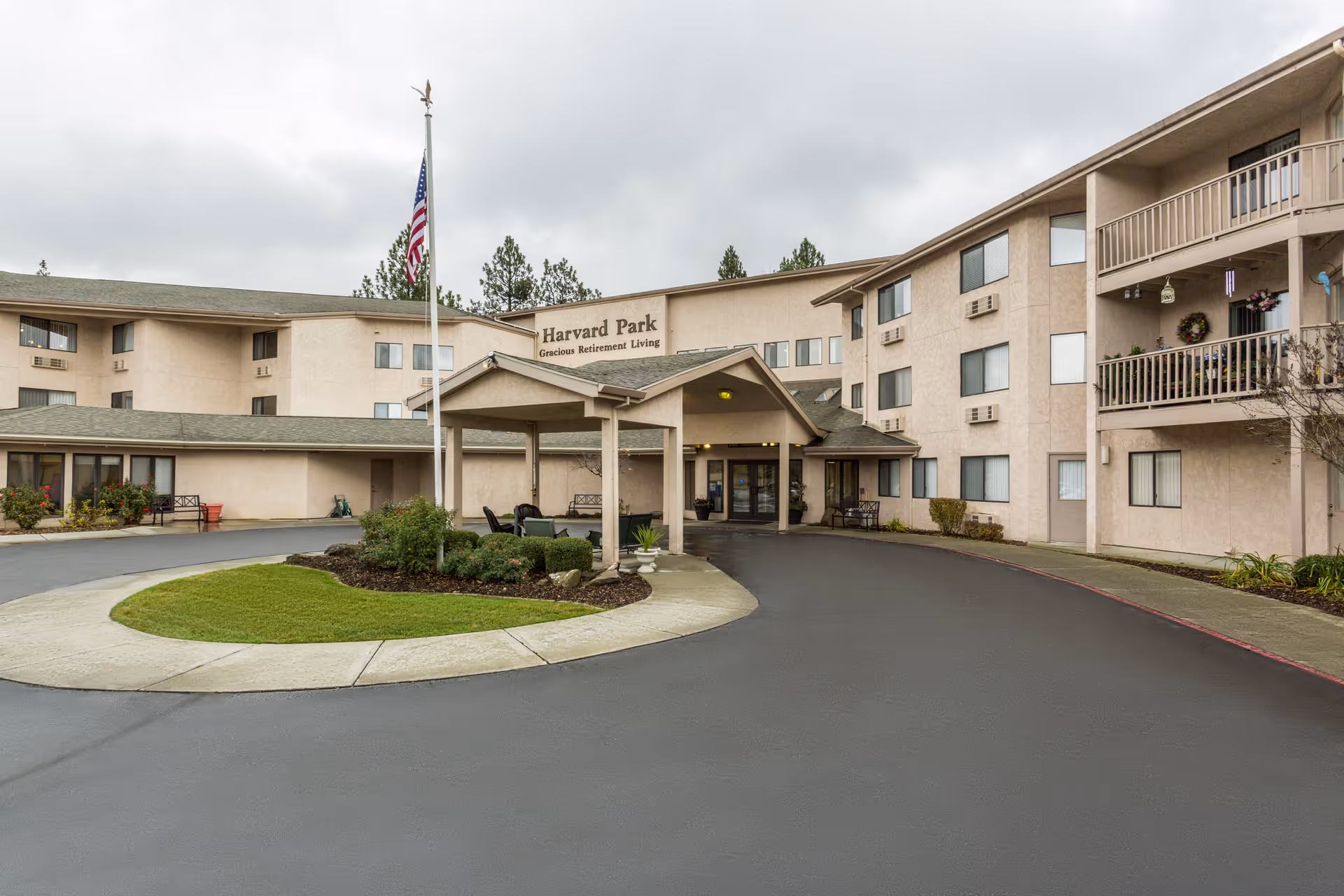 Front entrance and driveway of a multi-story retirement living building with a covered porte-cochere and an American flag.