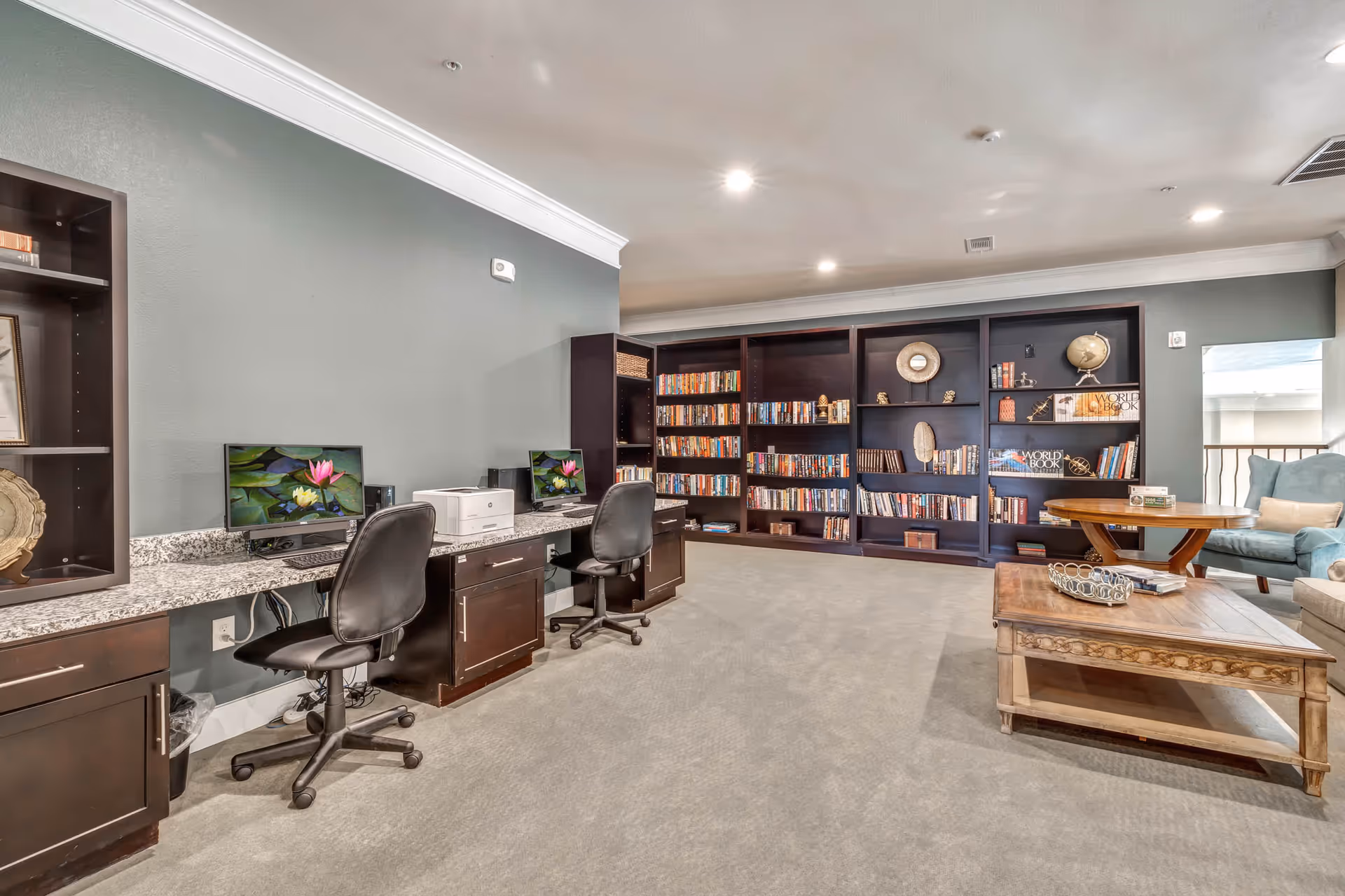 A comfortable lounge with computer workstations, large bookshelves, and seating including a coffee table and armchairs.