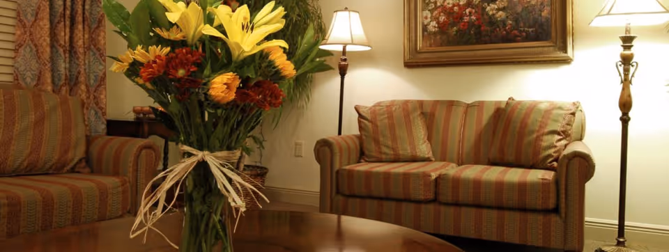 A cozy living room with striped sofas, a coffee table topped by a vase of flowers, floor lamps, and wall art.