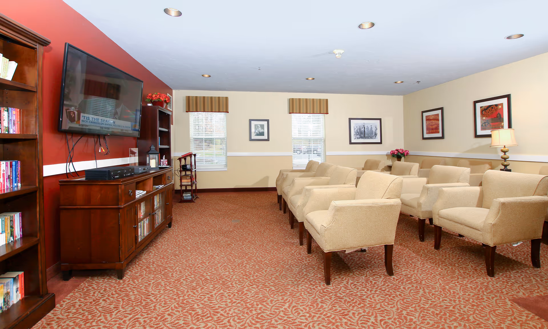 Community lounge with rows of beige armchairs facing a wall-mounted TV and wooden cabinetry.