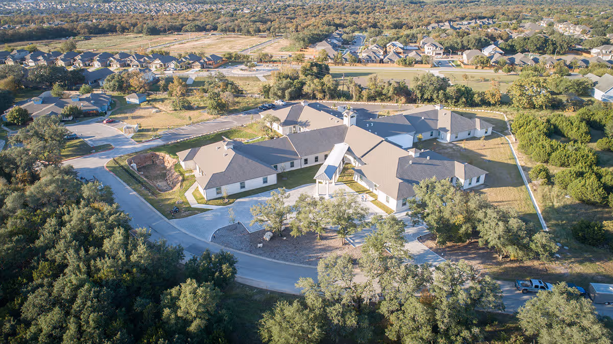 Aerial view of Provident at Buda facility surrounded by trees and residential houses, showing a large single-story building with multiple wings and a covered entrance.