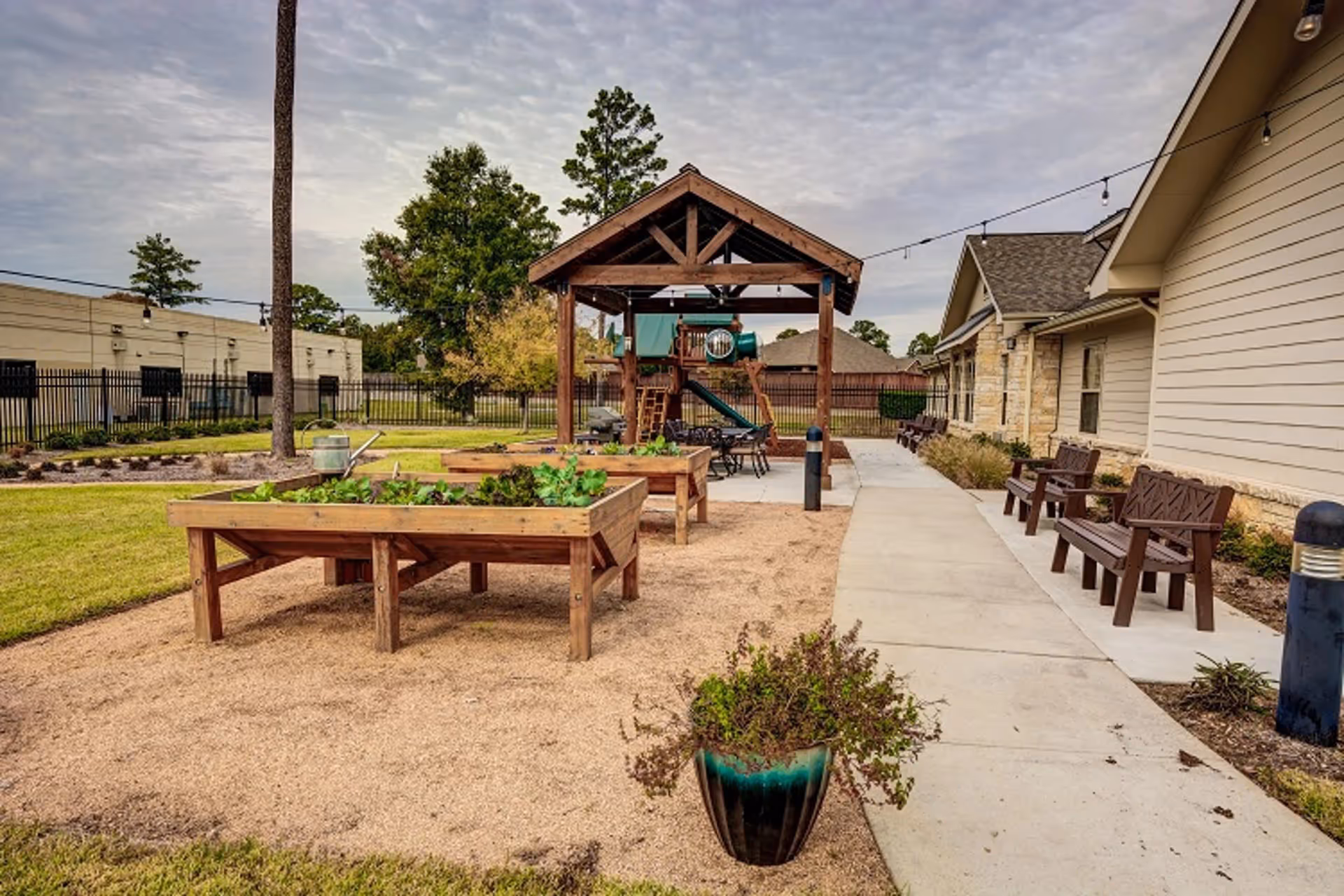 Outdoor courtyard with raised wooden garden beds, benches, a covered pavilion and a small playground next to the senior living building.
