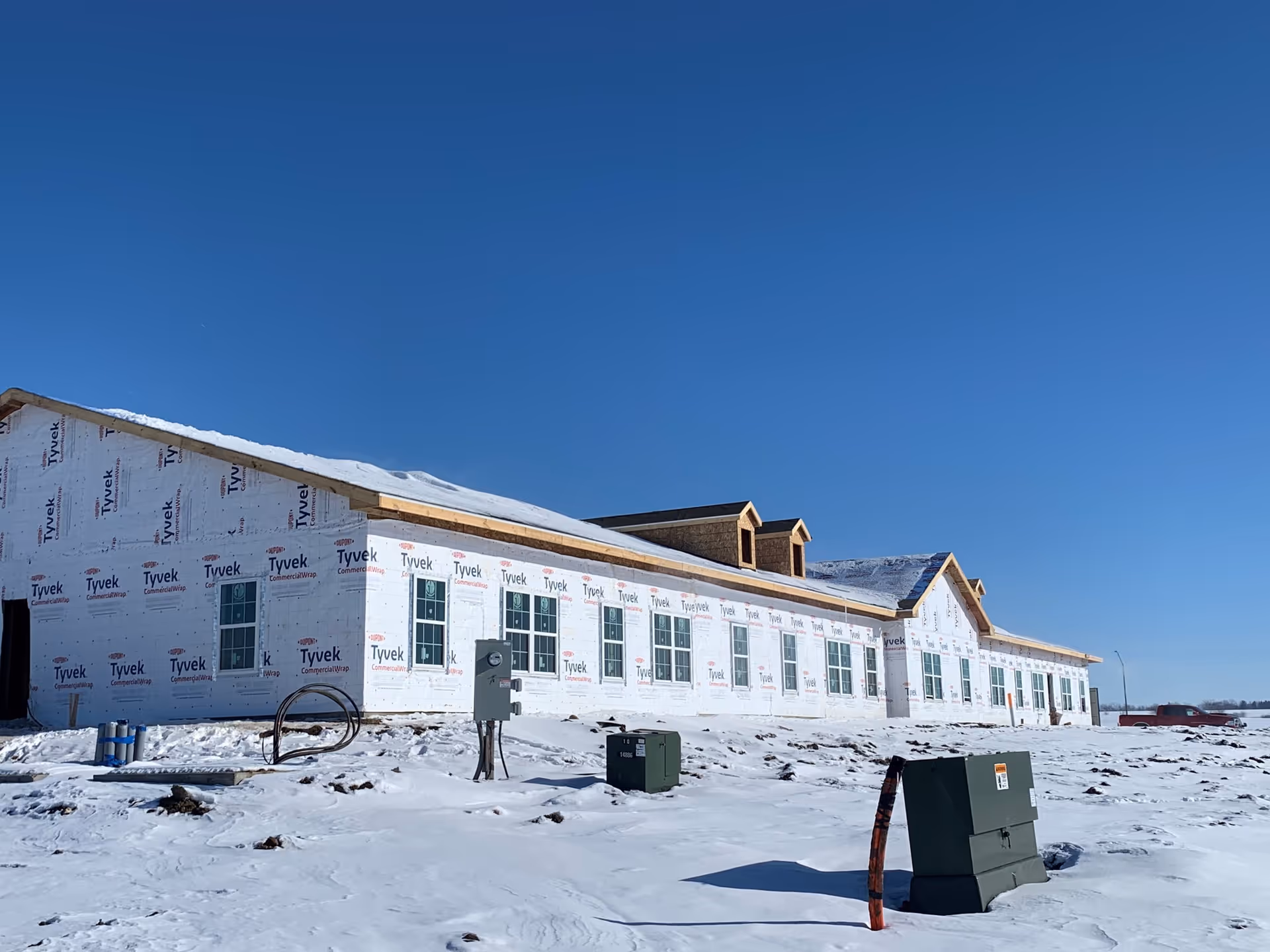 A large building under construction covered in Tyvek commercial wrap, surrounded by snow on the ground under a clear blue sky.
