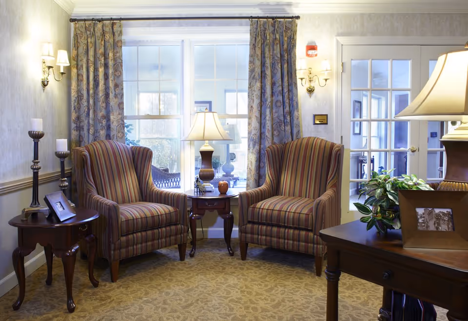 A cozy sitting area with two striped armchairs flanking a lamp-topped side table in front of a window and French doors.