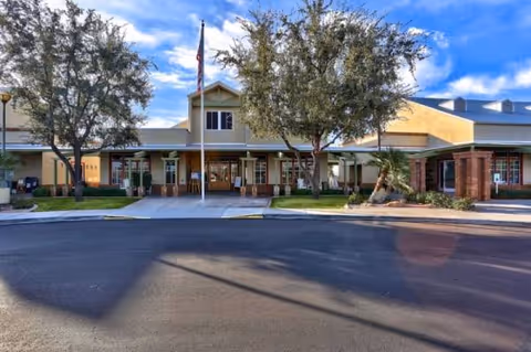 Front view of Arizona Traditions senior living facility with entrance, flagpole, and trees.